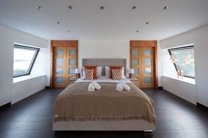 Une chambre spacieuse avec un grand lit, deux fenêtres et une vue sur l’extérieur.