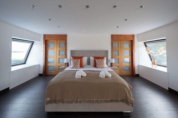A spacious bedroom with a large bed, two windows, and a view of the outdoors.