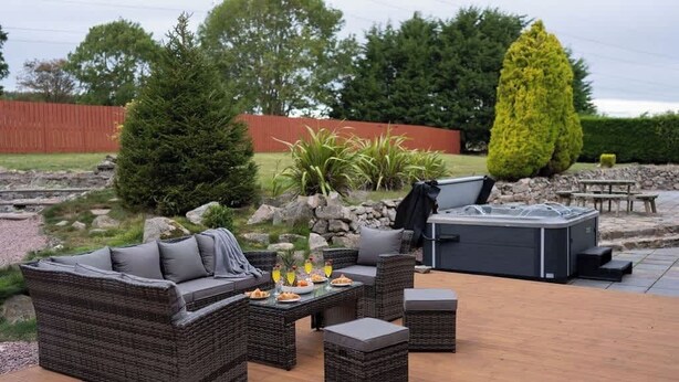 Une terrasse extérieure avec des meubles en osier, un jacuzzi et un mur en pierre.