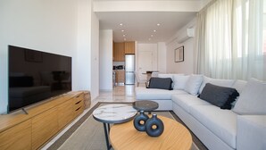 A modern living room with a flat-screen TV, a sofa, a coffee table, and a dining area in the background.