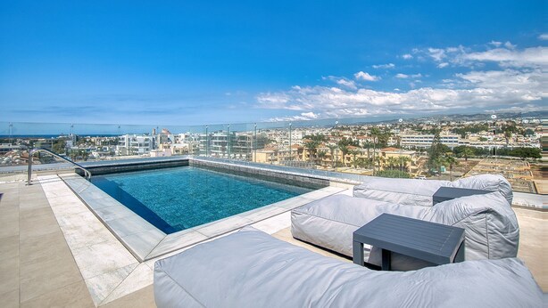 A rooftop pool with a city view, a covered seating area, and a clear sky.