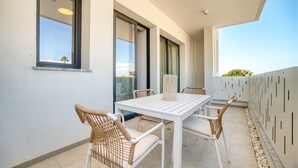 A balcony with a white table and wicker chairs, large windows, and a view of the cityscape.