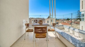A balcony with a table and chairs, overlooking a cityscape with buildings and a clear blue sky. - Arcadia 1 202 1 BED - One Bedroom Apartment, Sleeps 2 (Pafos)