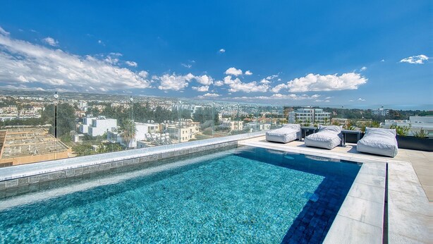 A rooftop infinity pool with clear blue water, surrounded by white cushioned seating and a glass railing. - Arcadia 1 202 1 BED - One Bedroom Apartment, Sleeps 2 (Pafos)