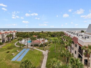 A resort with a pool, palm trees, and a view of the ocean. - Top-Floor Ocean & Pool View Condo | Steps to Beach (St. Augustine)