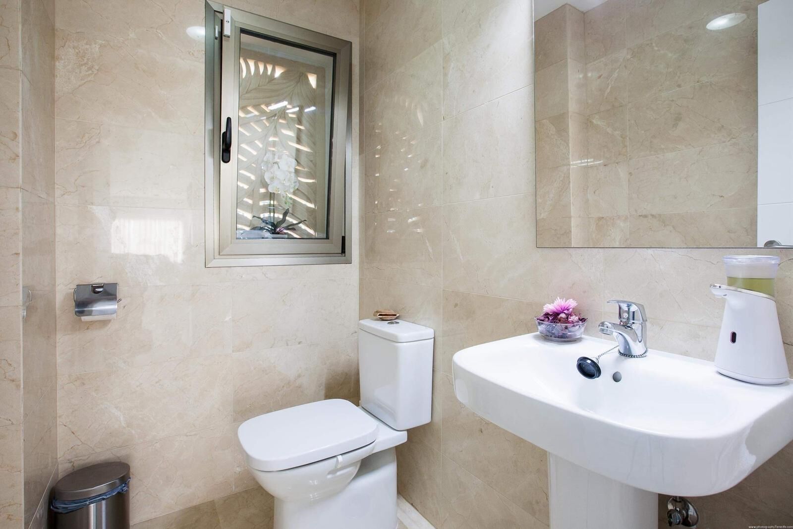 A bathroom with a toilet, a sink, and a window with a decorative screen.