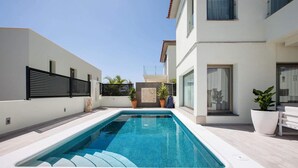 Un espace piscine moderne avec une piscine rectangulaire, des murs blancs et une clôture noire.