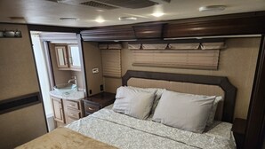 A compact RV bedroom with a bed, a small kitchenette, and a bathroom. - Cozy RV with WiFi and HVAC in Glendale/North Phoenix Luxury Fifth wheel camper (Glendale)