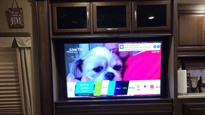 A living room with a flat-screen TV mounted on a wooden cabinet, a fireplace below, and a marble coffee table. - Cozy RV with WiFi and HVAC in Glendale/North Phoenix Luxury Fifth wheel camper (Glendale)