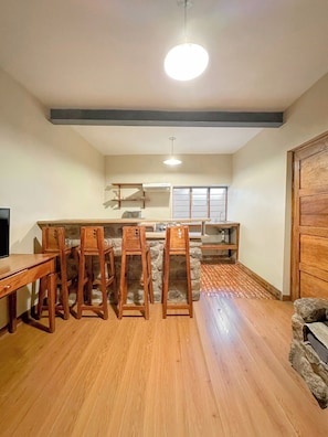 A dining area with wooden chairs and a table, a stone accent wall, a ceiling light, and a window with blinds. - Inka loft apartment in Cusco's historic center  (Cusco)