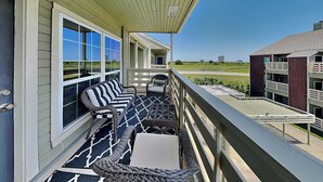 A balcony with wicker furniture, a patterned rug, and a view of a building and landscape. - Harbor East Condominiums 414D by Ryson Vacation Rentals (Galveston)