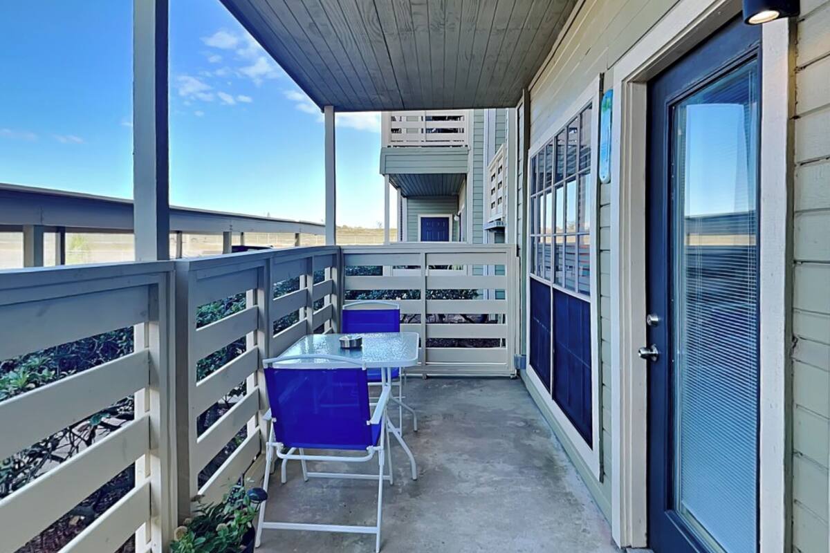 A covered outdoor area with a table and chairs, a door with a window, and a railing.
