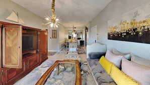 A living room with a sofa, a wooden cabinet, a chandelier, and a patterned rug. - Harbor East Condominiums 414D by Ryson Vacation Rentals (Galveston)