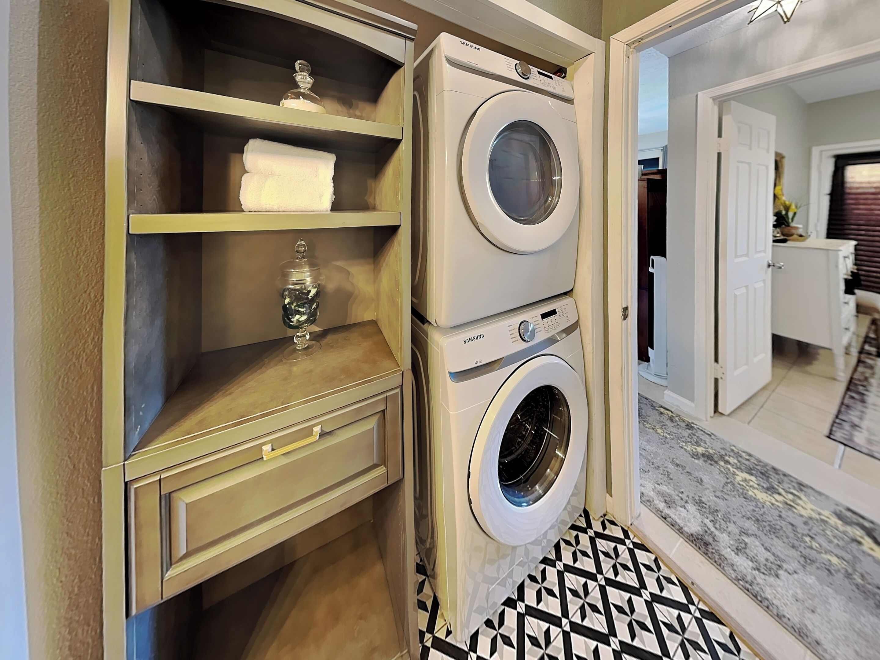 A laundry room with a Samsung washer and dryer, a shelf with towels, and a patterned floor.