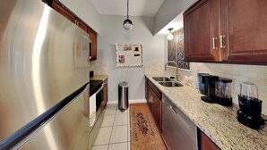 A kitchen with stainless steel appliances, granite countertops, wooden cabinets, and a backsplash. - Harbor East Condominiums 414D by Ryson Vacation Rentals (Galveston)