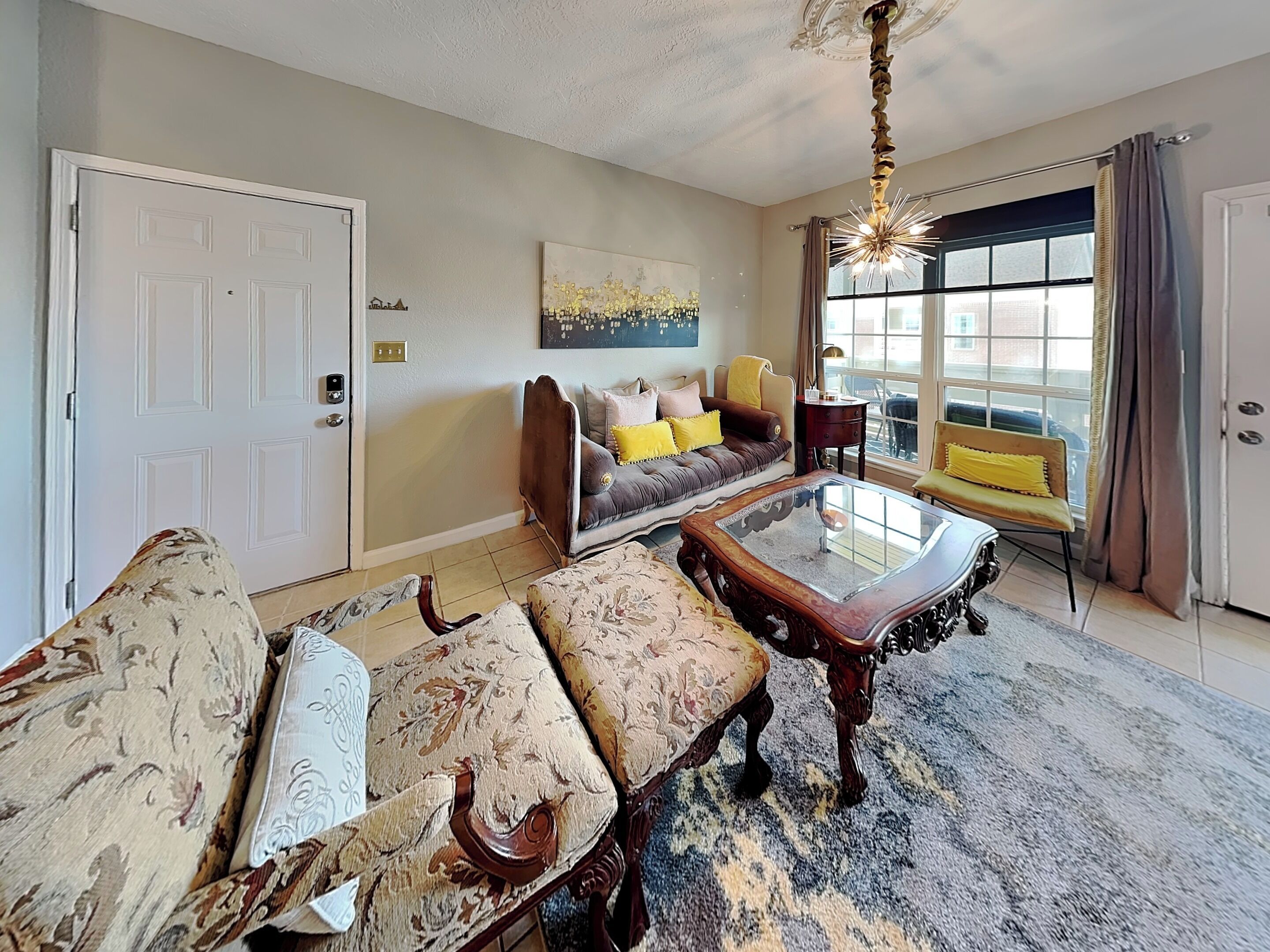 A living room with a sofa, armchair, coffee table, and a large window with curtains.