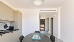 Une cuisine moderne dotée d’un plan de travail en marbre et de meubles de rangement, une table à manger avec des chaises, et une vue sur l’extérieur.