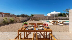 Un espace extérieur aménagé pour les repas, avec une table dressée pour deux personnes, une piscine et, au fond, un coin salon abrité.