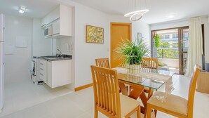 A modern kitchen with white cabinets, a dining area with a glass table and wooden chairs, and a view of the outdoors through a sliding glass door.