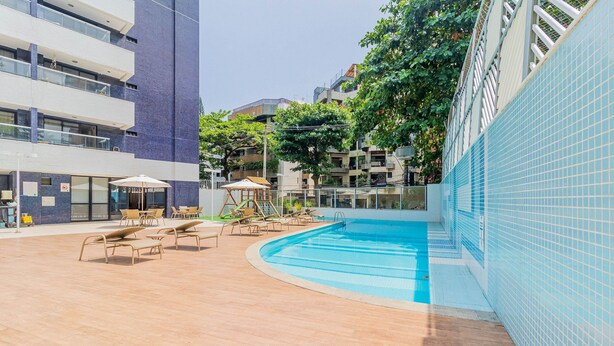 A rooftop pool area with lounge chairs and umbrellas, surrounded by buildings.