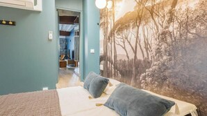 A bedroom with a bed, two pillows, a wall mural, and a door leading to another room. - NESTLED IN THE LIVELY AND CHARMING NOTRE-DAME-DES-CHAMPS DISTRICT- RUE DE SEVRES (Paris)