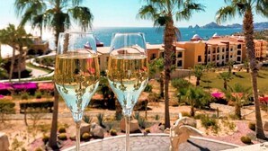 Deux verres de vin blanc sur une table, avec vue sur un complexe hôtelier et l’océan.