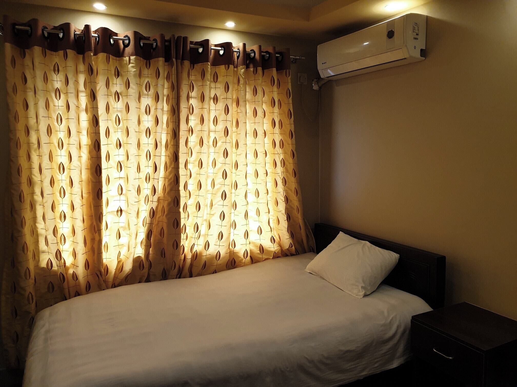 Une chambre d’hôtel comprenant un lit, une table de chevet, un appareil de climatisation et des rideaux à motifs de feuilles.