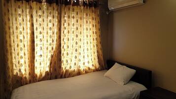 Une chambre d’hôtel comprenant un lit, une table de chevet, un appareil de climatisation et des rideaux à motifs de feuilles.