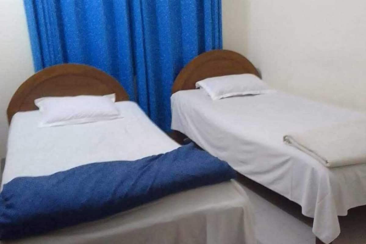 Deux lits simples avec des têtes de lit en bois et du linge de lit blanc, séparés par un rideau bleu.
