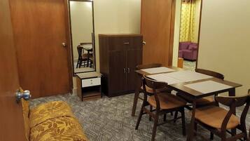 A compact room with a bed, a wardrobe, a small table with chairs, and a mirror.