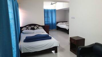 Quarto de hotel com uma cama, uma cadeira, uma mesinha e uma janela com cortinas.