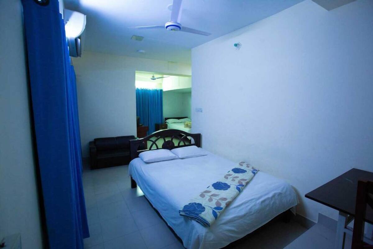 Une chambre à coucher comprenant un lit, un bureau, une chaise, un ventilateur de plafond et une fenêtre avec des rideaux.
