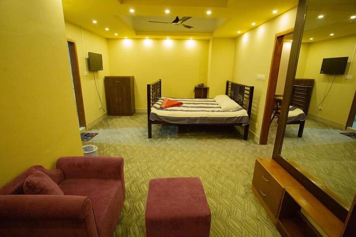 Une pièce comprenant un lit, deux chaises, un miroir et un ventilateur de plafond.