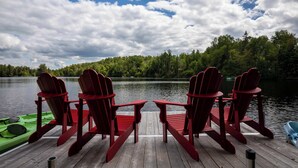 A wooden dock with four red Adirondack chairs facing a calm lake, surrounded by dense forest.