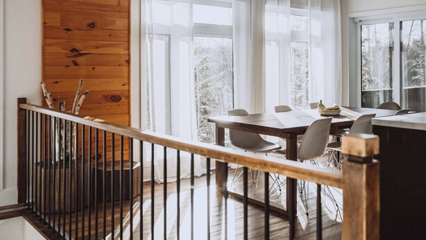 A modern interior with a wooden ceiling, a dining area with a table and chairs, and a view of trees outside.