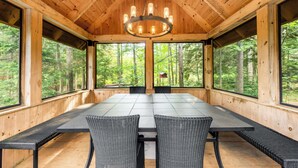 A wooden cabin with a large dining table and chairs, large windows, and a chandelier.