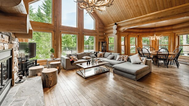 A spacious living room with a fireplace, large windows, and a wooden ceiling.