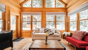 L’intérieur d’un chalet accueillant, avec un décor en bois, un canapé, un divan rouge et une table basse agrémentée d’un vase de fleurs.