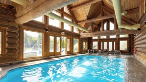 A log cabin with a large indoor swimming pool, wooden beams, and large windows.
