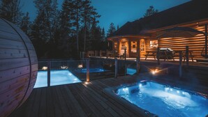 A wooden cabin with a hot tub and a pool, surrounded by trees.