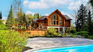 A log cabin with a swimming pool, surrounded by lush greenery and trees.