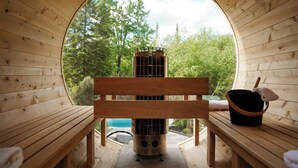 A sauna room with a wooden bench, a sauna heater, and a bucket.