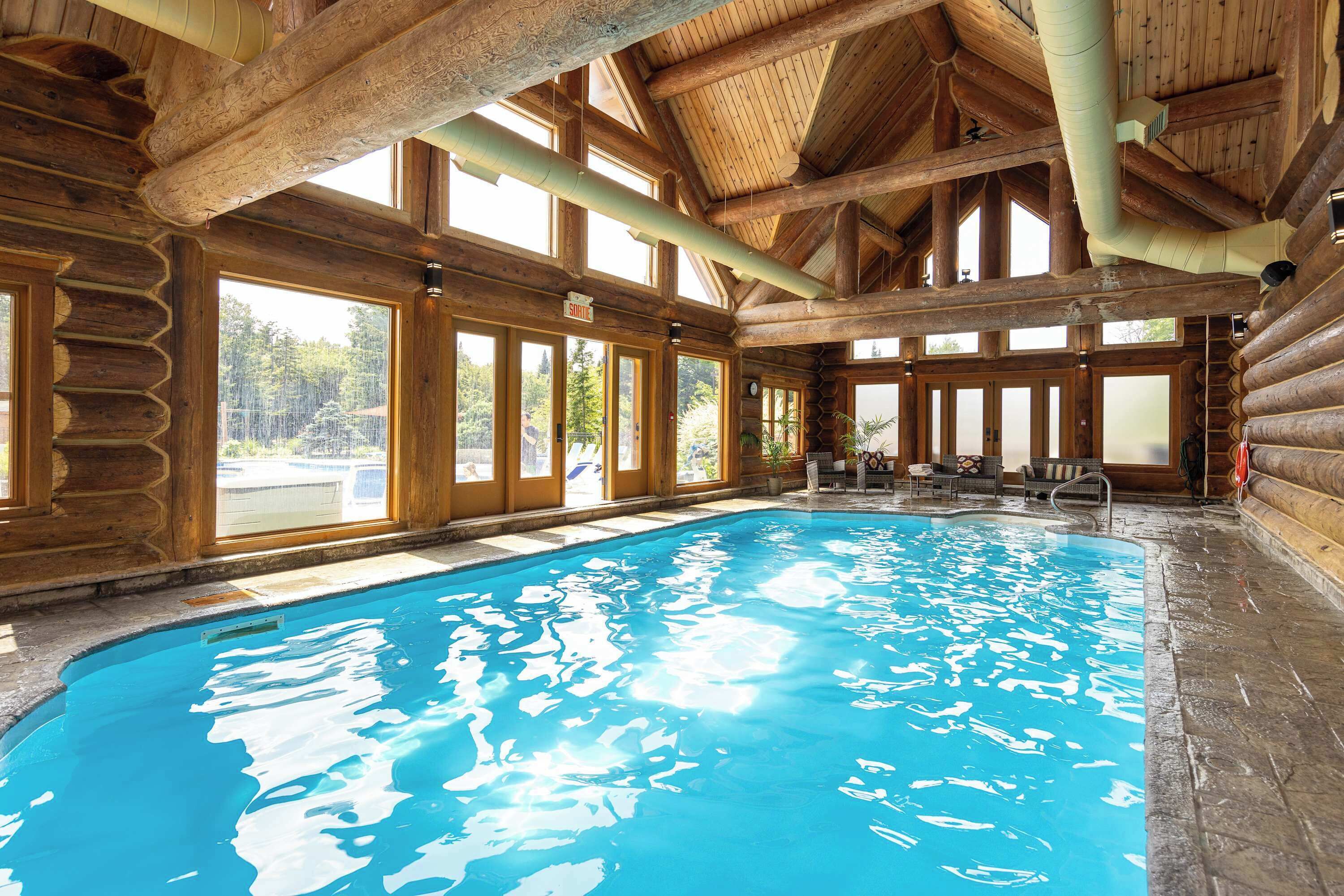 Una cabaña de troncos con una amplia piscina interior, vigas de madera y grandes ventanales.