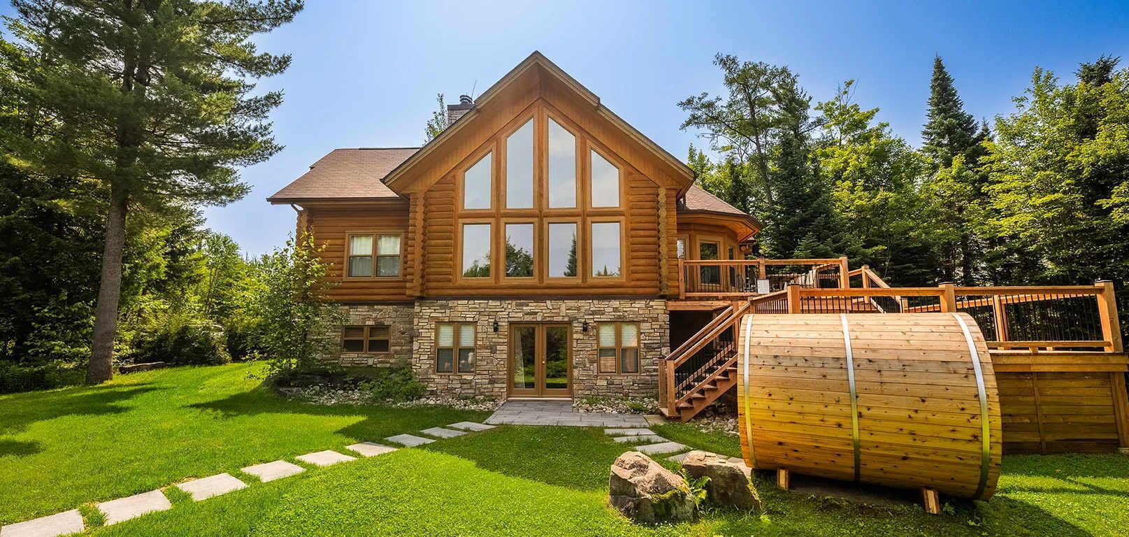 Una cabaña de troncos con cimientos de piedra, ventanas grandes y una terraza de madera.