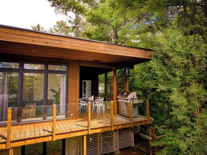 Eine Holzterrasse mit Sitzgelegenheiten und Grill, umgeben von Bäumen.