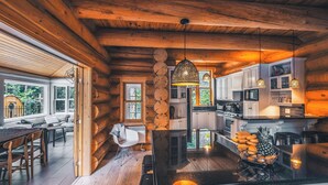 A log cabin interior with a kitchen, dining area, and a large window. - Chalet Silver Fox at Fiddler Lake with Hot Tub, Sauna, and Private Pool (Mille-Isles)