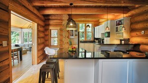 A log cabin interior with a kitchen featuring white cabinets, a black countertop, and hanging pendant lights. - Chalet Silver Fox at Fiddler Lake with Hot Tub, Sauna, and Private Pool (Mille-Isles)