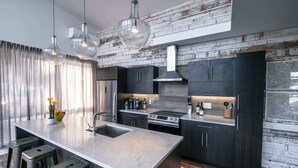 Uma cozinha moderna com armários escuros, uma ilha grande com banquetas e iluminação pendente.