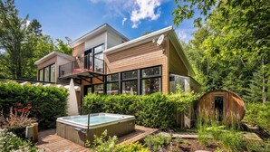 Uma casa moderna de dois andares com hidromassagem, deck de madeira e uma construção semelhante a uma cabana no jardim.