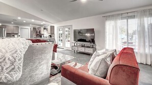 A modern living room with a red sofa, a glass coffee table, and a flat-screen TV. - Mesa Lake Front House With Pool and Hot Tub! (Mesa)